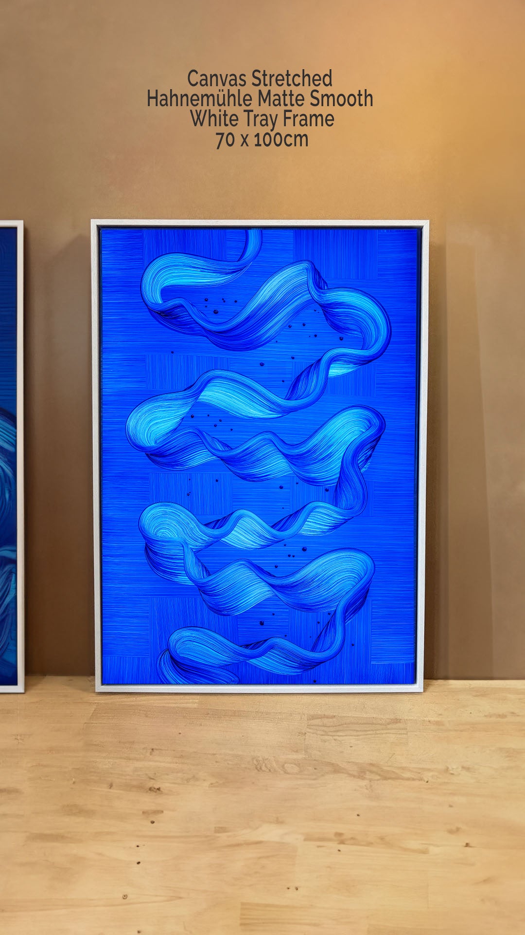 Ebb and Flow abstract art by Lara Sayegh, featuring ocean-inspired rhythmic brushstrokes, printed on canvas stretched in a white floater tray frame on a wooden floor with a brown wall background.