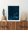 Framed abstract blue wave artwork on a wooden console table with decorative plants.