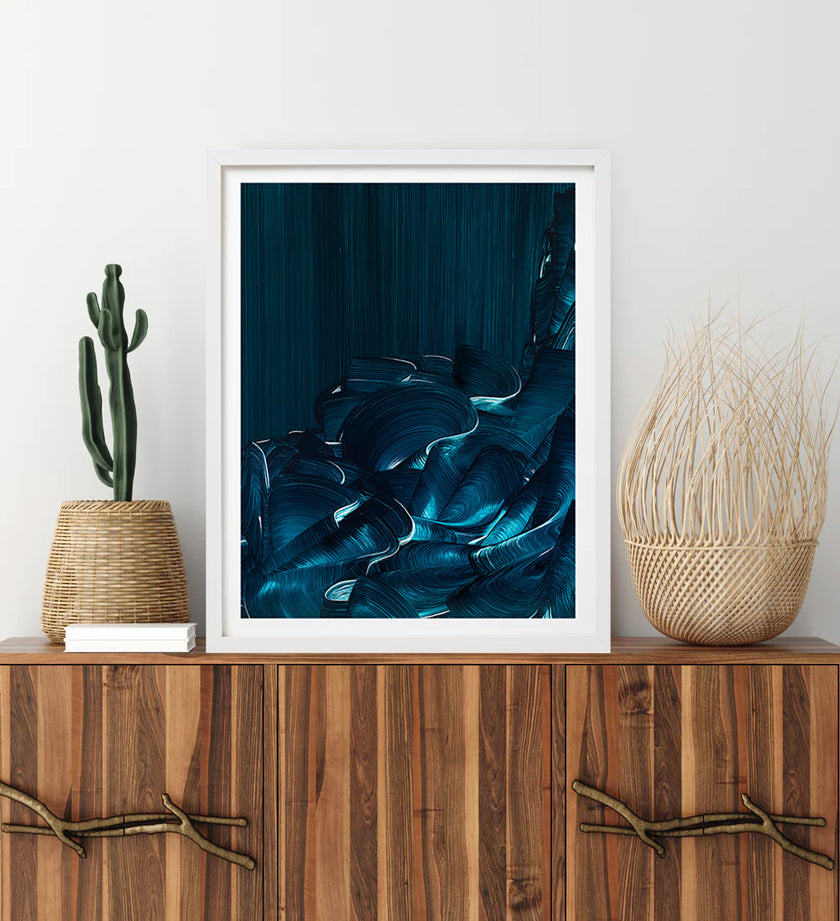 Framed abstract blue wave artwork on a wooden console table with decorative plants.