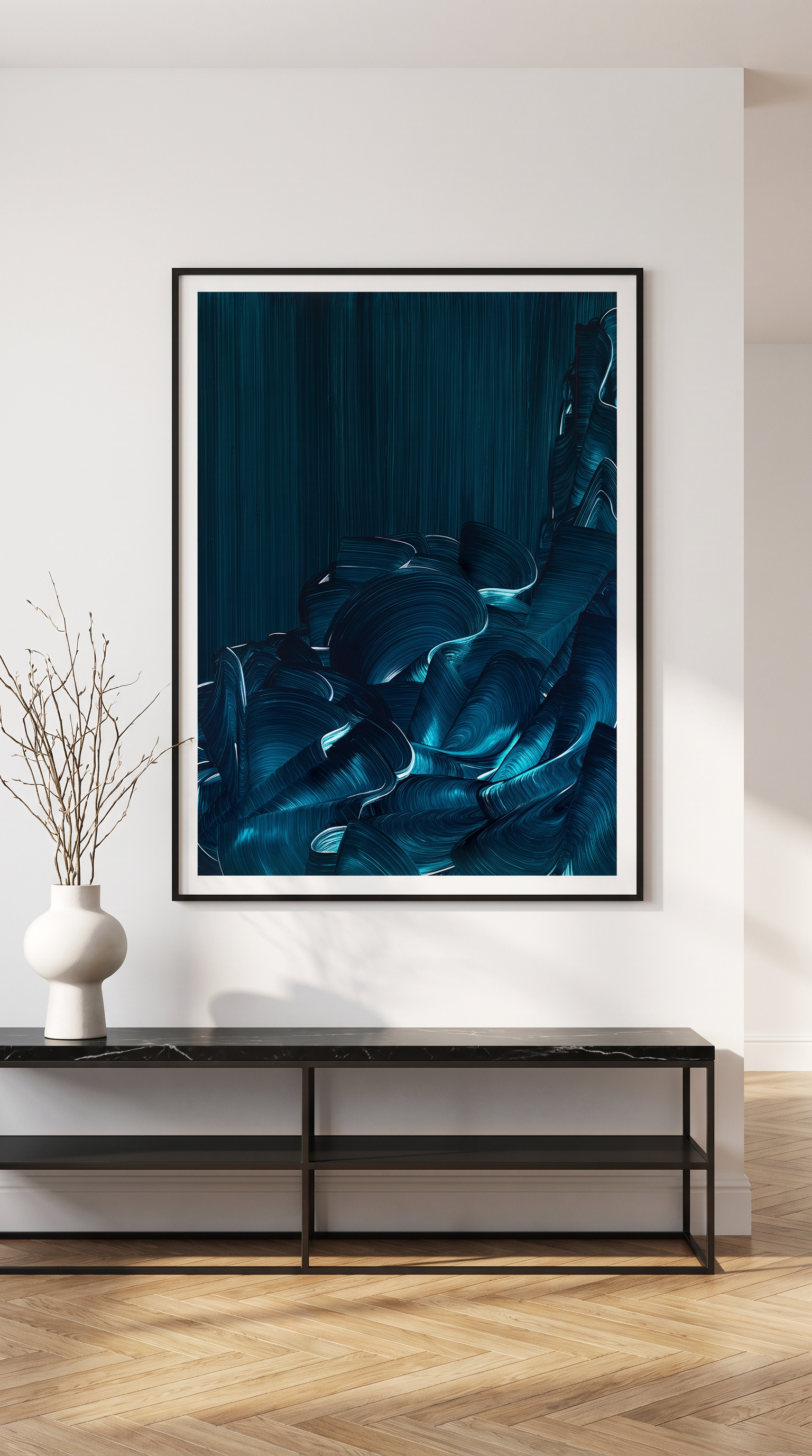 A framed abstract art print featuring deep teal and blue textured brushstrokes, displayed on a white wall above a black console table with a white vase of branches.